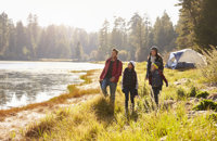 Family walking along river with tent in background