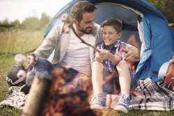 Father and son sitting together next to campfire, toasting marshmallows