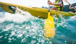 Close shot of explorer women in life jacket paddling hard the kayak with splashes