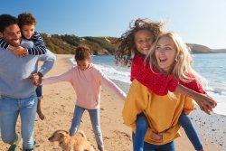 arents Giving Children Piggybacks As They Walk Along Beach