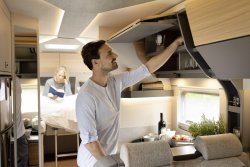 Man in motorhome kitchen area with woman in background reading