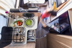 Birds-eye view of motorhome kitchen with food prep on the side and girl looking in fridge.