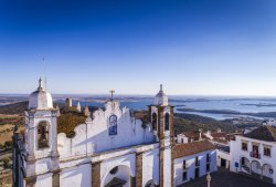 Aerial view of a church facade in the historic village of Monsaraz in Alentejo with the Alqueva dam reservoir on the background; Concept for travel in Portugal and Alentejo and most beautiful places in Portugal
