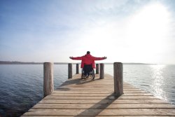 Man in wheelchair overlooking lake with arms out