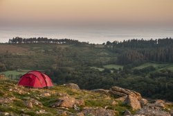 Red tent on rocky outcrop overlooking hazy scenery
