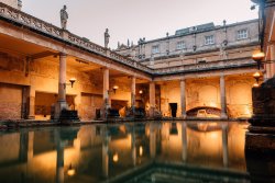 A low angle shot of the Roman Baths at dusk with atmospheric lights around the baths.