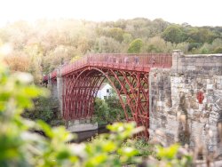 Atmospheric image of the iconic red Iron Bridge at Ironbridge Gorge with green foliage in foreground.